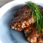 Delicious sausage patties garnished with fresh dill, placed on a blue plate, capturing the savory and appetizing appearance of the dish.