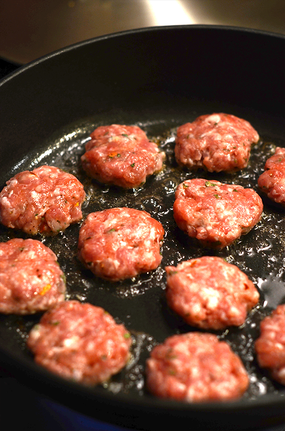 Mini sage sausage patties in a cast iron pan being cooked