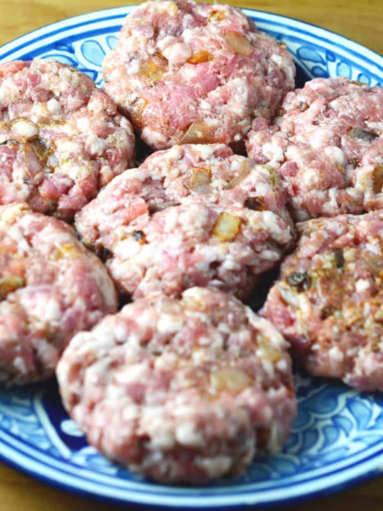 Close-up of raw pork burger patties mixed with onions, neatly arranged on a blue plate, ready for cooking.