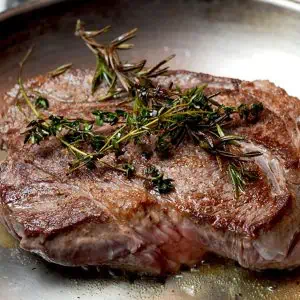 Close-up of a tender boneless beef chuck roast garnished with caramelized onions and mushrooms, plated with chives on top.
