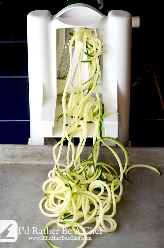 Zoodles recipe going through the spiralizer. Note that the pan below is a half sheet pan which you will need to catch all the zoodles!