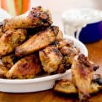 A plate of crispy baked chicken wings with a bowl of blue cheese dip in the background. The wings are perfectly golden and look incredibly appetizing, with a focus on their crispy texture.