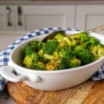 Close-up of roasted broccoli florets in a white dish, sprinkled with red pepper flakes, with a spoon resting inside the dish.