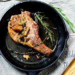 A perfectly seared pork chop with garlic and rosemary in a black cast iron skillet.