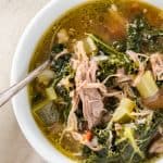Overhead view of a bowl of pulled pork soup with kale and vegetables, garnished with a spoon.