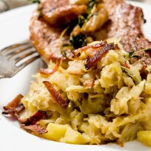 A detailed view of sautéed cabbage with crispy bacon and a fork on a white plate.