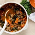 Close-up of Tuscan kale soup showcasing the hearty vegetables and sausage in a savory broth, with a spoon inside the white bowl.