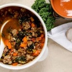 White bowl of Tuscan kale soup next to kale