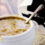 A close-up view of a white bowl filled with rich, golden French onion soup, topped with a layer of melted cheese, and a spoon resting inside.