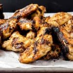A mouth-watering close-up of grilled chicken wings, highlighting their crispy, golden skin and savory charred spots, arranged on a parchment-lined tray.