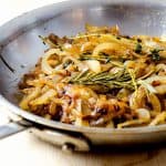 Close-up of caramelized onions with rosemary and thyme in a skillet, highlighting the rich brown color and texture.
