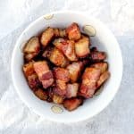 Close-up of crispy lardon (cubed bacon) in a white bowl, emphasizing its rich and crispy texture.