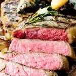 Sliced medium-rare Porterhouse steak served with grilled mushrooms and rosemary on a wooden cutting board.