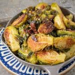 Overhead view of roasted Brussels sprouts mixed with crispy bacon bits in a cast iron skillet, with sea salt scattered around.