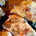 Close-up of perfectly roasted chicken pieces with golden-brown, crispy skin, seasoned with salt and pepper, arranged on a wooden cutting board.