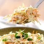 Close-up of a spoonful of coleslaw with shredded cabbage and carrots in a creamy dressing being lifted above a bowl, garnished with parsley.