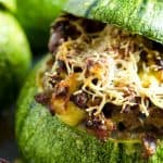 stuffed zucchini topped with shredded cheese served in a zucchini