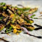 Close-up of crispy zucchini fries drizzled with balsamic glaze, garnished with fresh basil and thinly sliced red onions on a light grey surface.