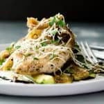 sauteed chicken breast topped with shredded cheese and fresh herbs served on a plate