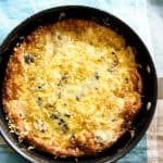 An overhead view of a golden-brown mushroom and leek frittata in a black pan.