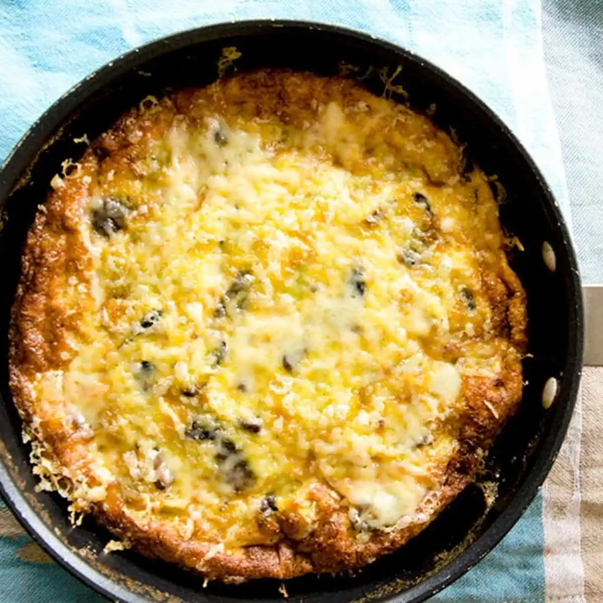 An overhead view of a golden-brown mushroom and leek frittata in a black pan.