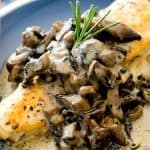 Close-up of stuffed chicken breast covered in creamy mushroom gravy and garnished with a fresh rosemary sprig, ready to be enjoyed.