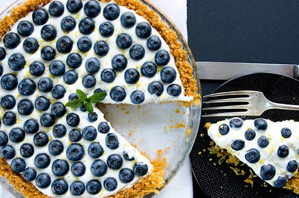 No bake cheesecake with a thin layer of vanilla whipped cream, lemon zest and fresh blueberries.