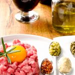 Steak tartare  served in a plate and accompanied by spoonfuls of toppings and seasonings