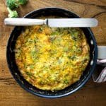 Perfectly cooked broccoli cheddar frittata in a skillet, with a golden-brown top and hints of green from the broccoli, on a wooden table.