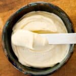 Overhead view of smooth, homemade mayo with a spatula in a blue bowl.