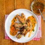 Overhead view of lemon garlic chicken wings on a white plate with sauce on a wooden table.