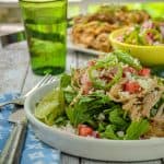 A vibrant salad featuring slow-cooked pork carnitas on a bed of mixed greens, topped with chopped onions, tomatoes, and jalapenos, garnished with crumbled cheese and lime wedges.