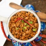 A bowl of homemade Mexican chorizo garnished with a dried red chili and fresh cilantro, served on a colorful patterned coaster.