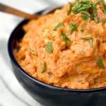 Close-up of a bowl of carrot mash with ginger and garlic, garnished with chopped herbs.