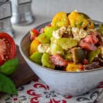 A bowl of vibrant Tomato Feta Salad served on a patterned cloth, next to a cutting board with sliced tomato
