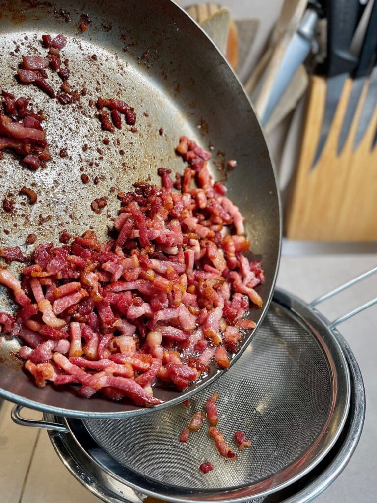 Cooked bacon bits being transferred to a drainage system out of a pan