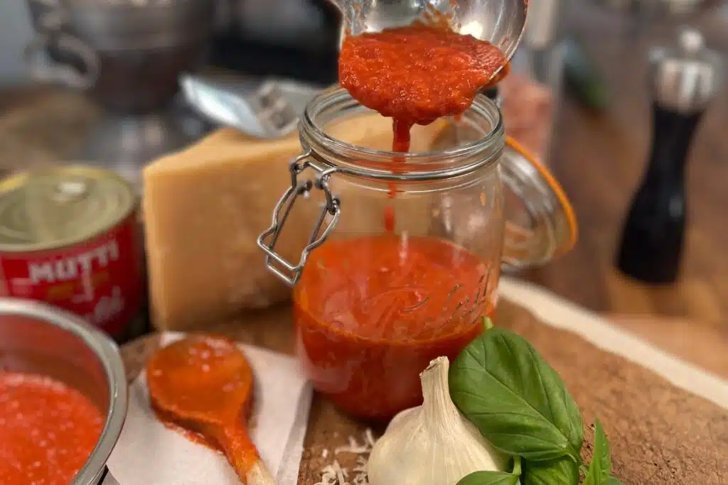 Homemade tomato sauce being added to a mason jar