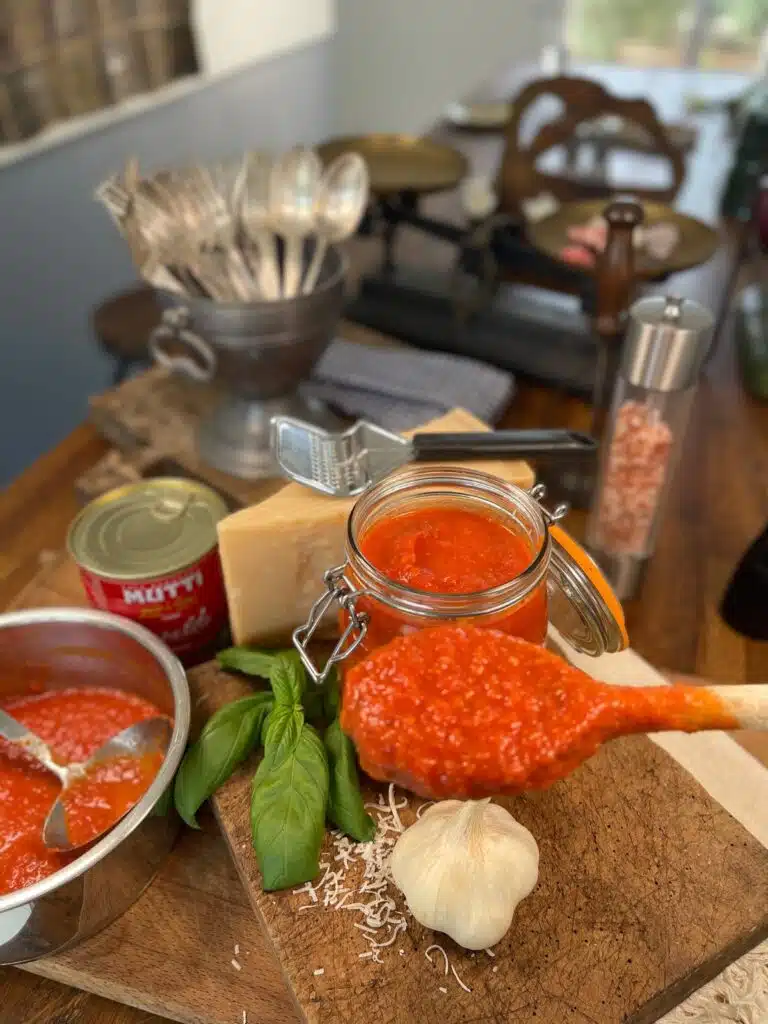 Spoonful of homemade tomato sauce held over jar and bowl of sauce