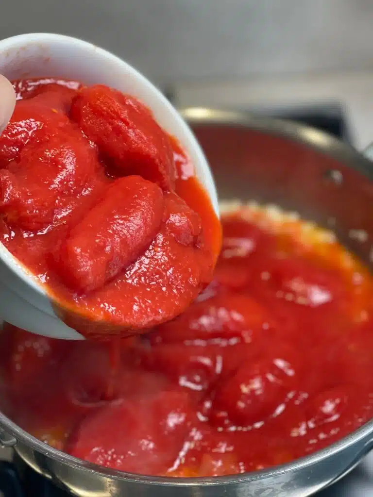 Tomatoes and sauce being added to a pan