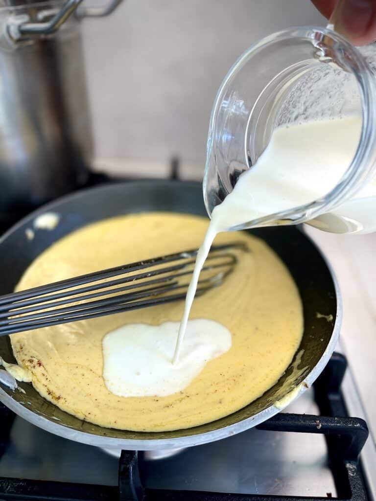 Adding cream to the melted cheese mixture in a frying pan.