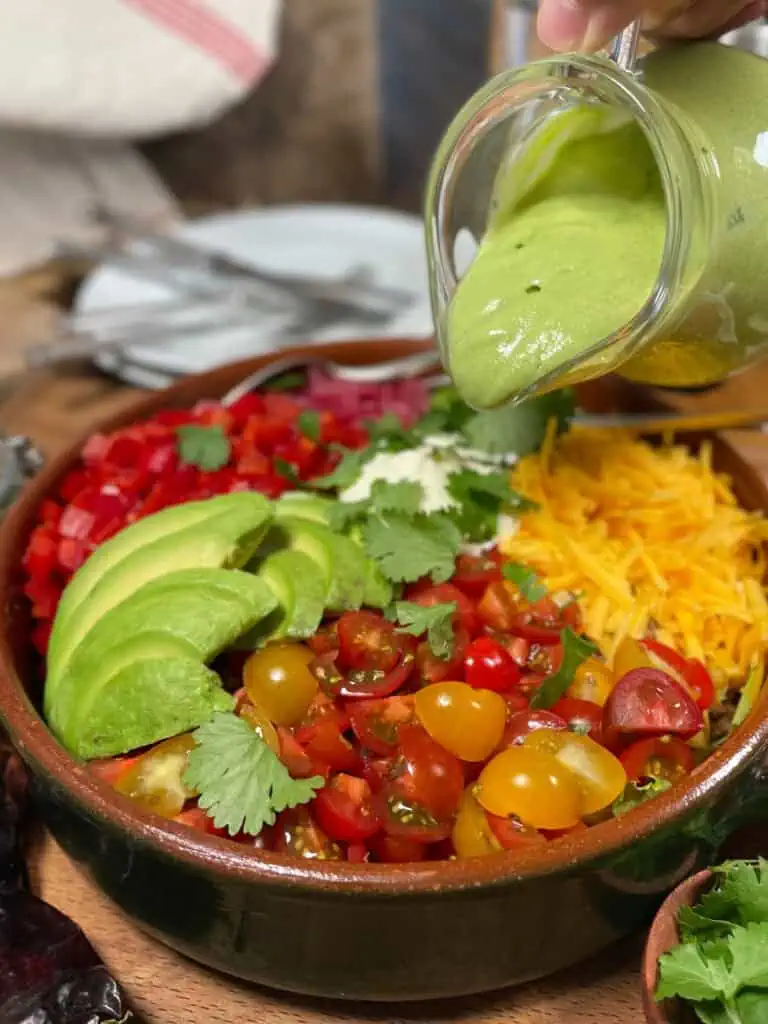 Avocado lime dressing being poured onto a mixed salad