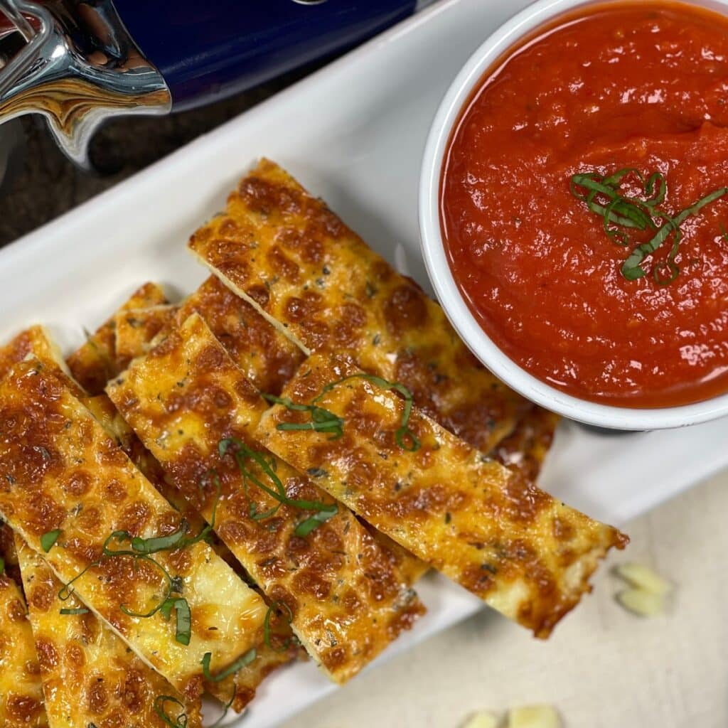 Cheesy keto breadsticks served with sauce and garnished with fresh herbs