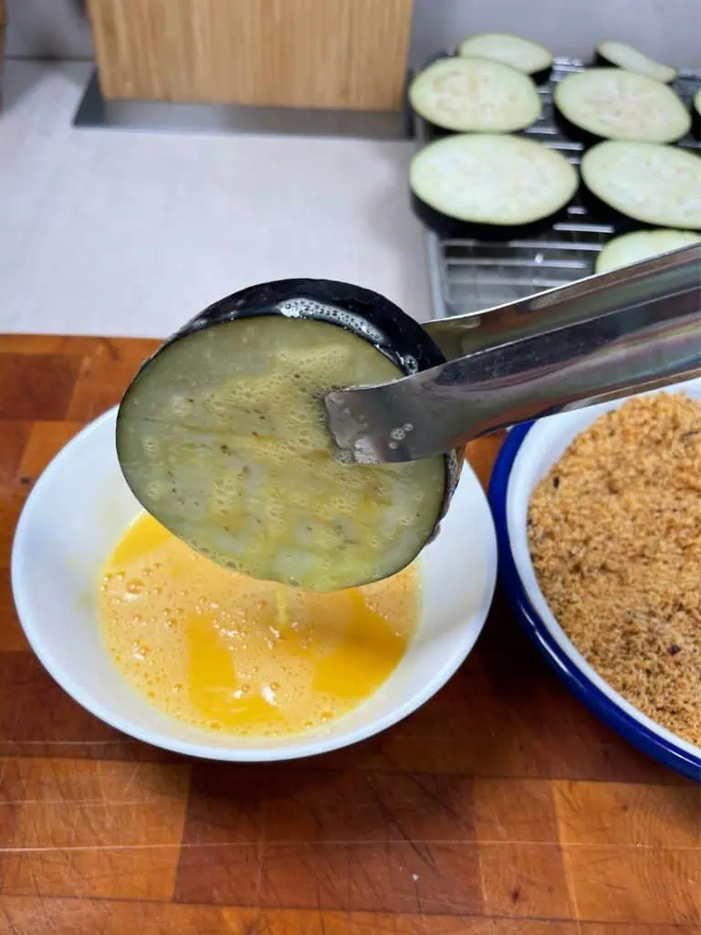 Eggplant being dipped into raw egg in preparation for keto eggplant parmeasan