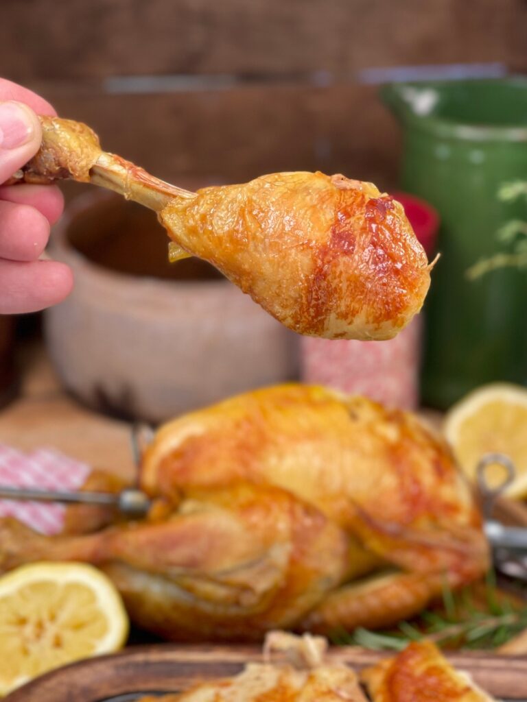 Leg of rotisserie chicken being held obver the chicken