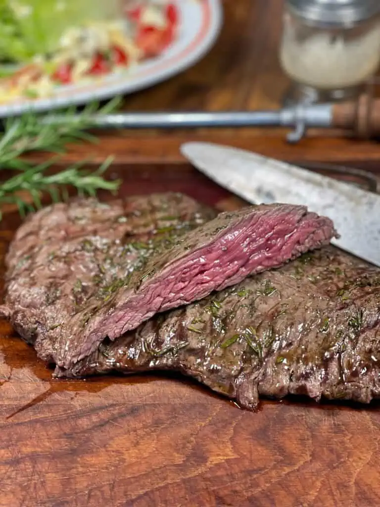 Sliced steak marinade served with fresh herbs on a cutting board