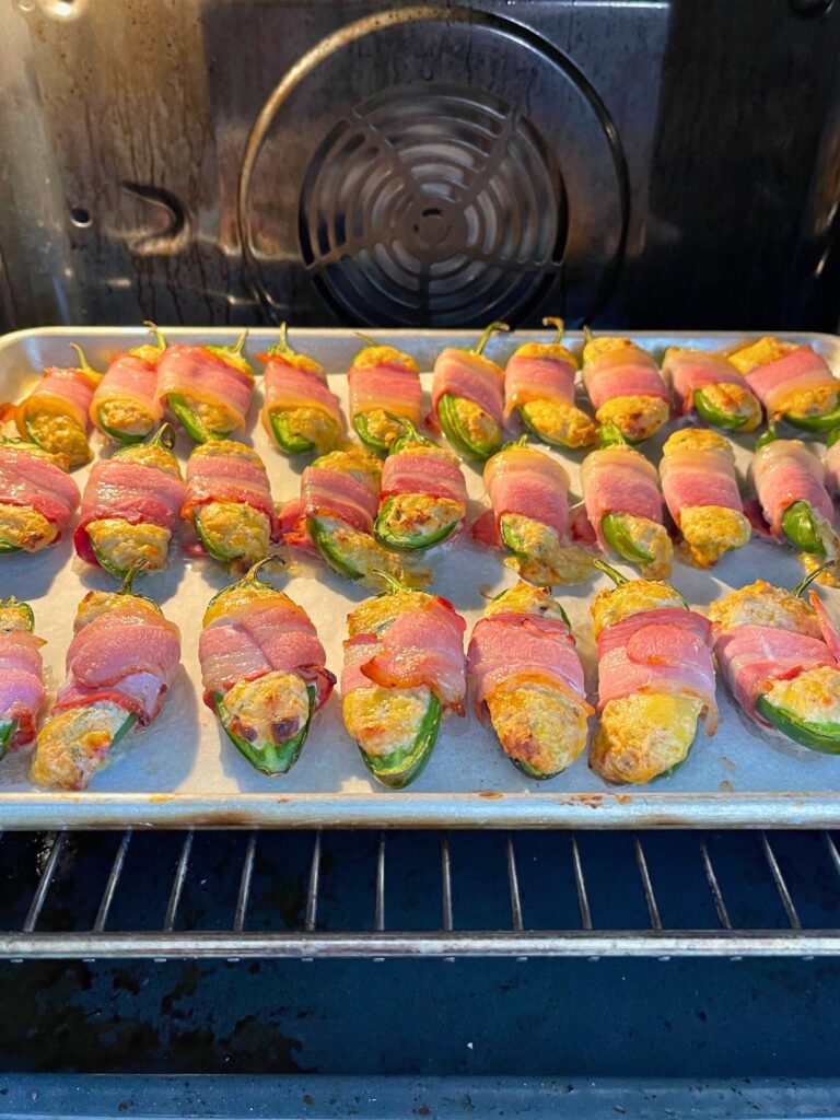 Uncooked bacon wrapped jalapeño poppers baking in oven