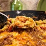 A close-up of a cheesy Brussels sprouts casserole with a spoon lifting a portion, showcasing the melted cheese and crispy, golden-brown topping.