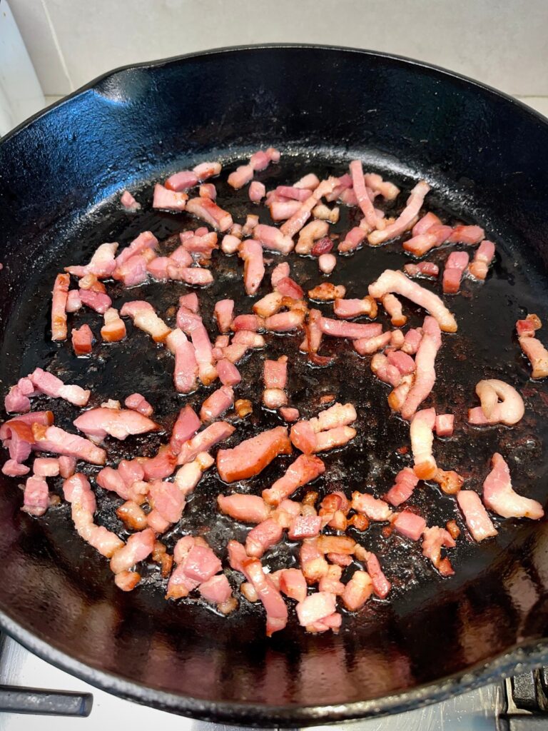 Bacon bits sizzling in a pan for cheesy Brussels sprout casserole
