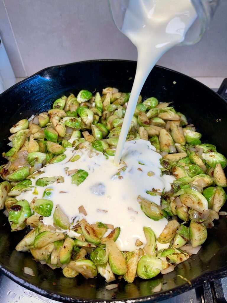 Ingredients being added and cooked in a pan for cheesy Brussels sprout casserole
