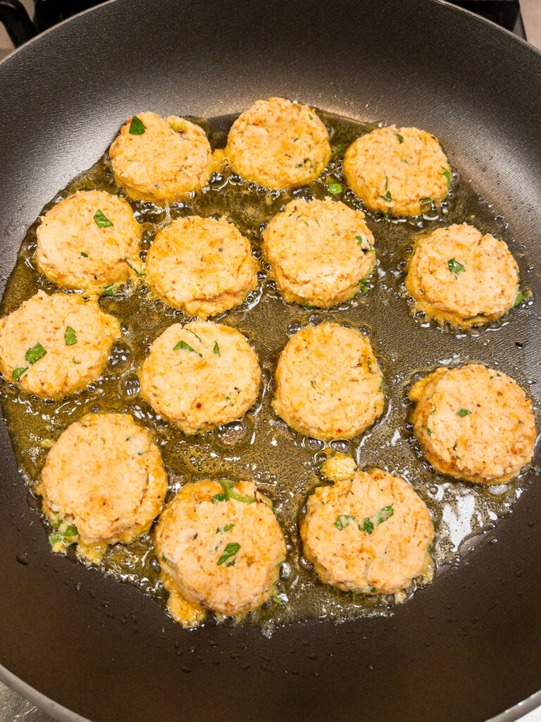 keto crab cakes being seared in a pan with fresh herbs